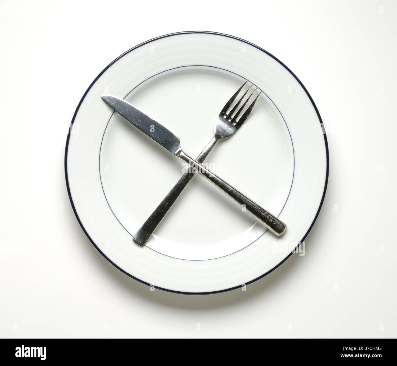 Une assiette blanche ronde avec un couteau et fourchette croisés. Banque D'Images