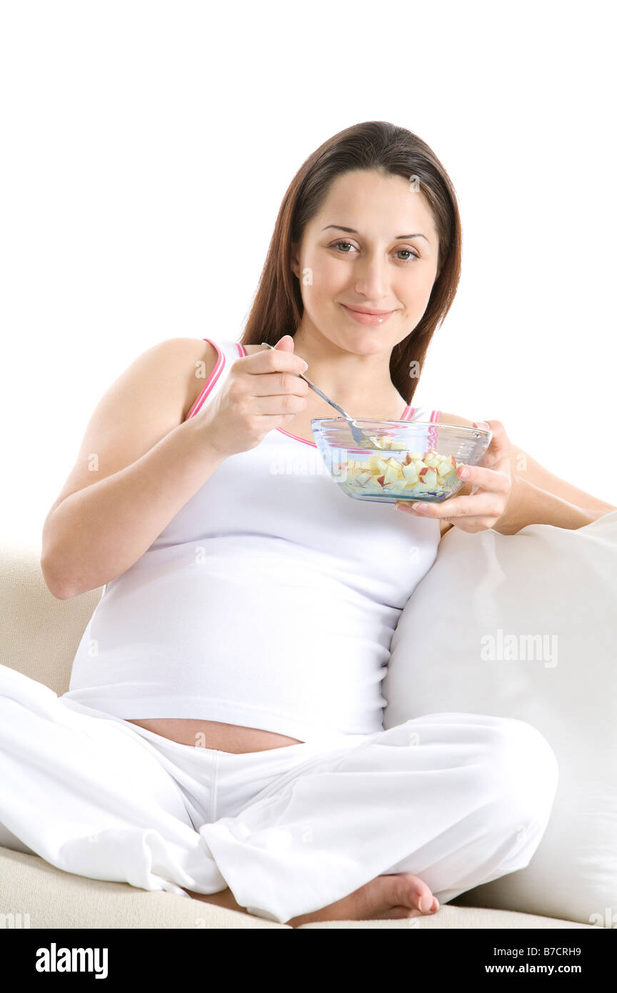 Jeune femme enceinte de manger un bol sitting on sofa Banque D'Images