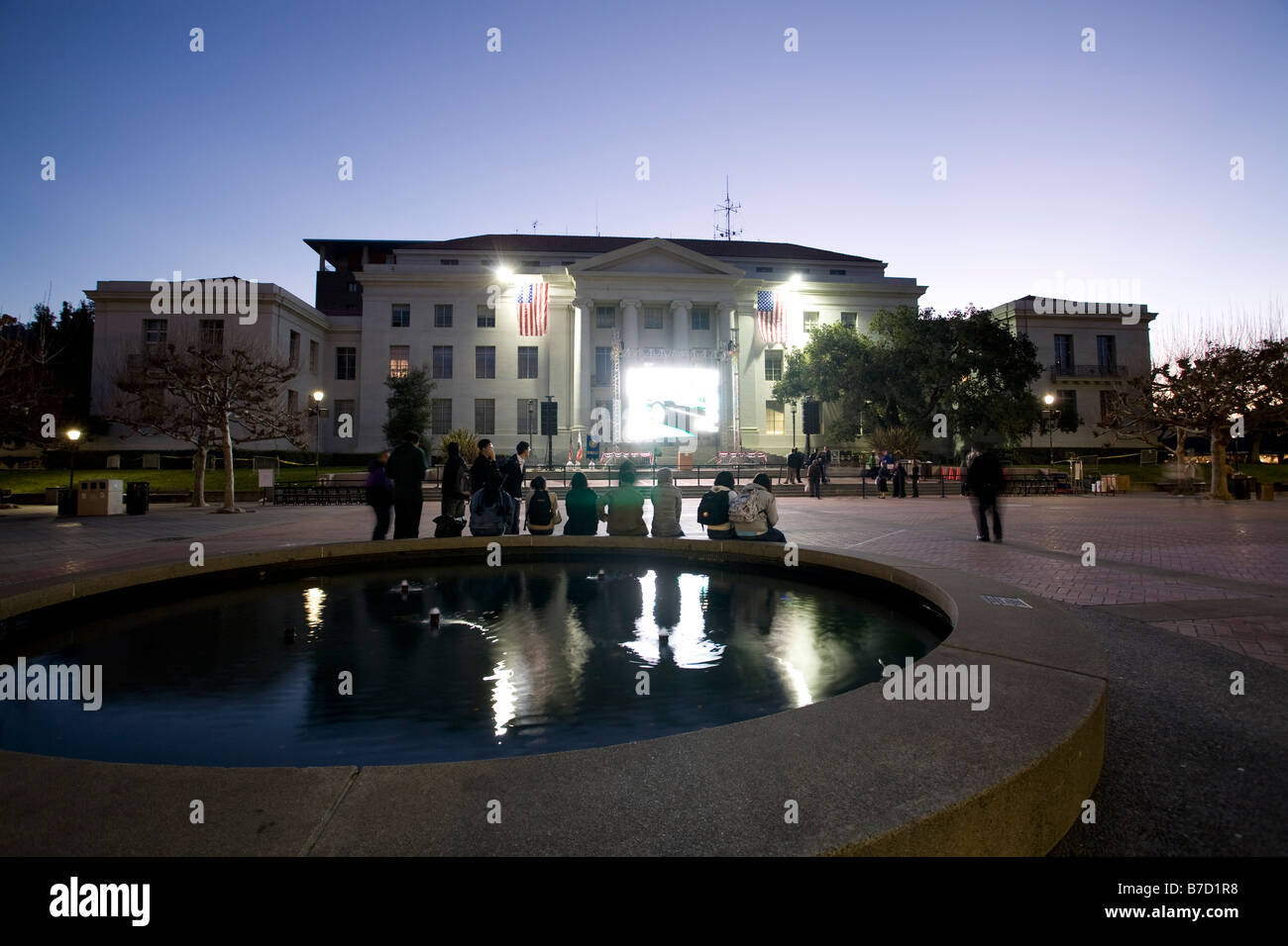Les étudiants et les résidents s'asseoir sur Sproul fontaine à l'Université de Californie à regarder la couverture de l'inauguration. Banque D'Images