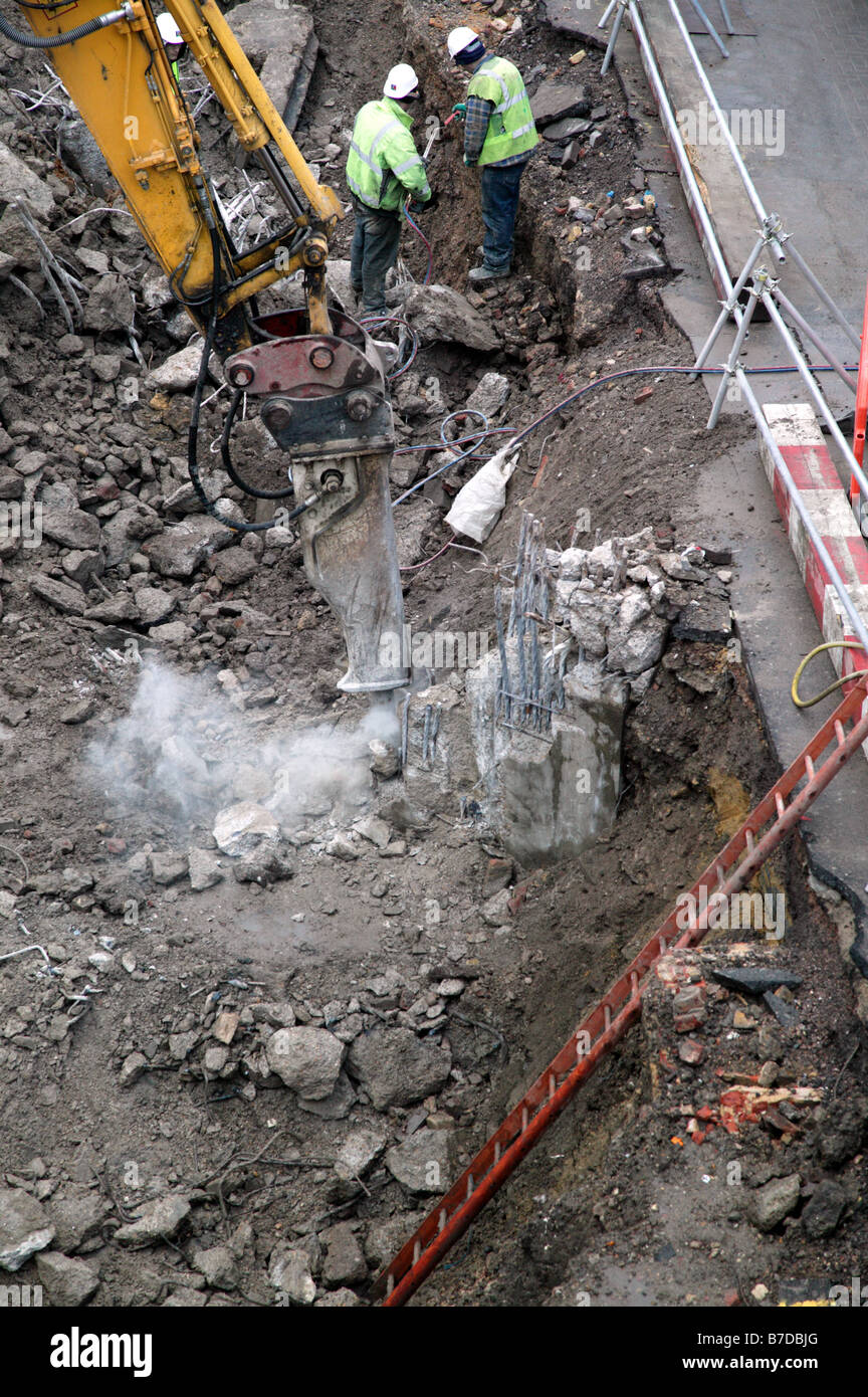 À l'aide d'un marteau hydraulique ouvrier attaché à un excavateur pour briser les restes d'un pilier en béton armé Banque D'Images