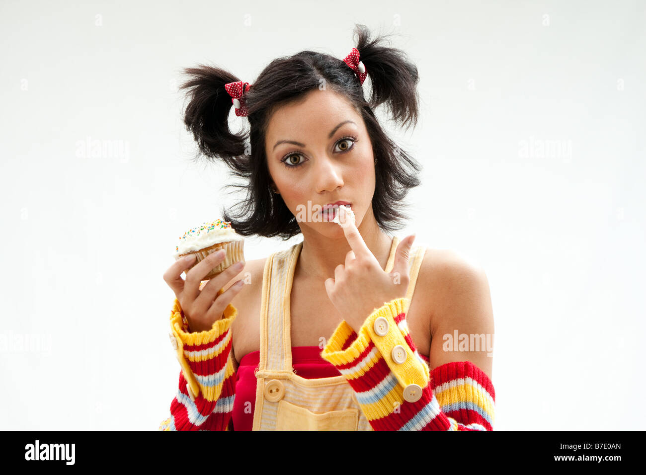 Belle Latina girl eating a cupcake avec ses doigts et lui lécher ses lèvres couvertes de glace isolé Banque D'Images