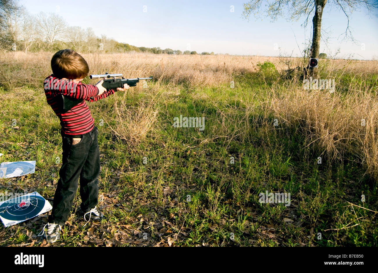 Jeune garçon avec son fusil à plombs attentivement par la portée de son arme en vue d'une cible fixée à une arborescence distante Banque D'Images