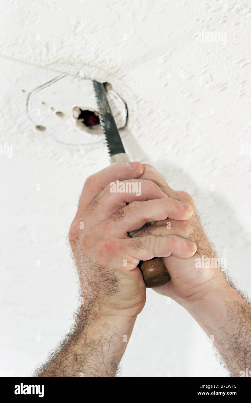 Un électricien avec l'aide d'une scie à découper un trou dans le plafond pour mettre un ventilateur fort travail est effectué par un élu maître Banque D'Images