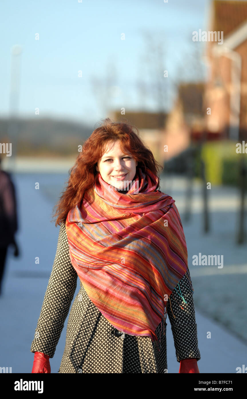Jeune femme aux cheveux rouges, vêtus de manteau, gants et écharpe sur une journée froide mais lumineuse. Banque D'Images