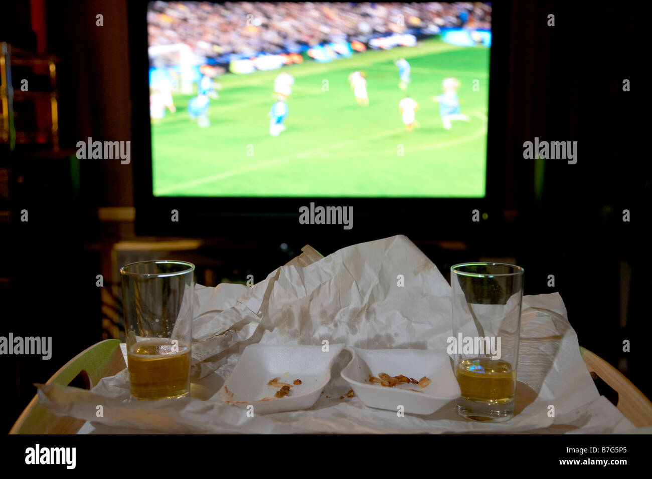 Restes d'un repas à emporter pour deux et verres de bière sur un plateau en face de soccer sur la télévision dans le salon d'une maison Banque D'Images