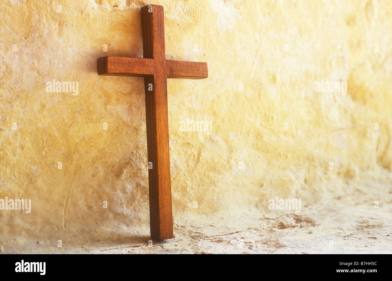 Petit crucifix en bois debout dans une lumière chaude contre mur peint crème dans fenêtre Banque D'Images