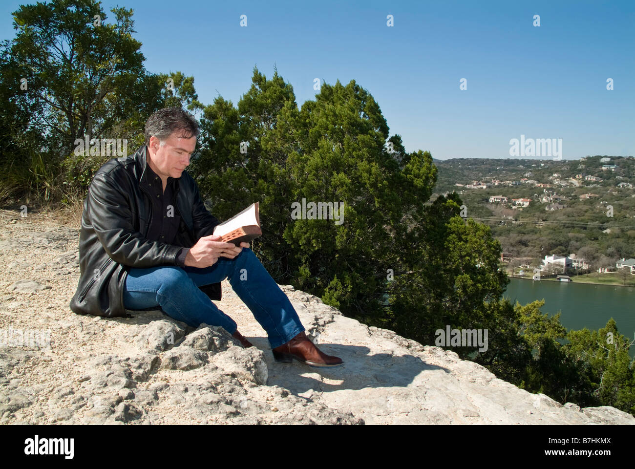 Un homme assis sur une barre rocheuse de lire une Bible Banque D'Images