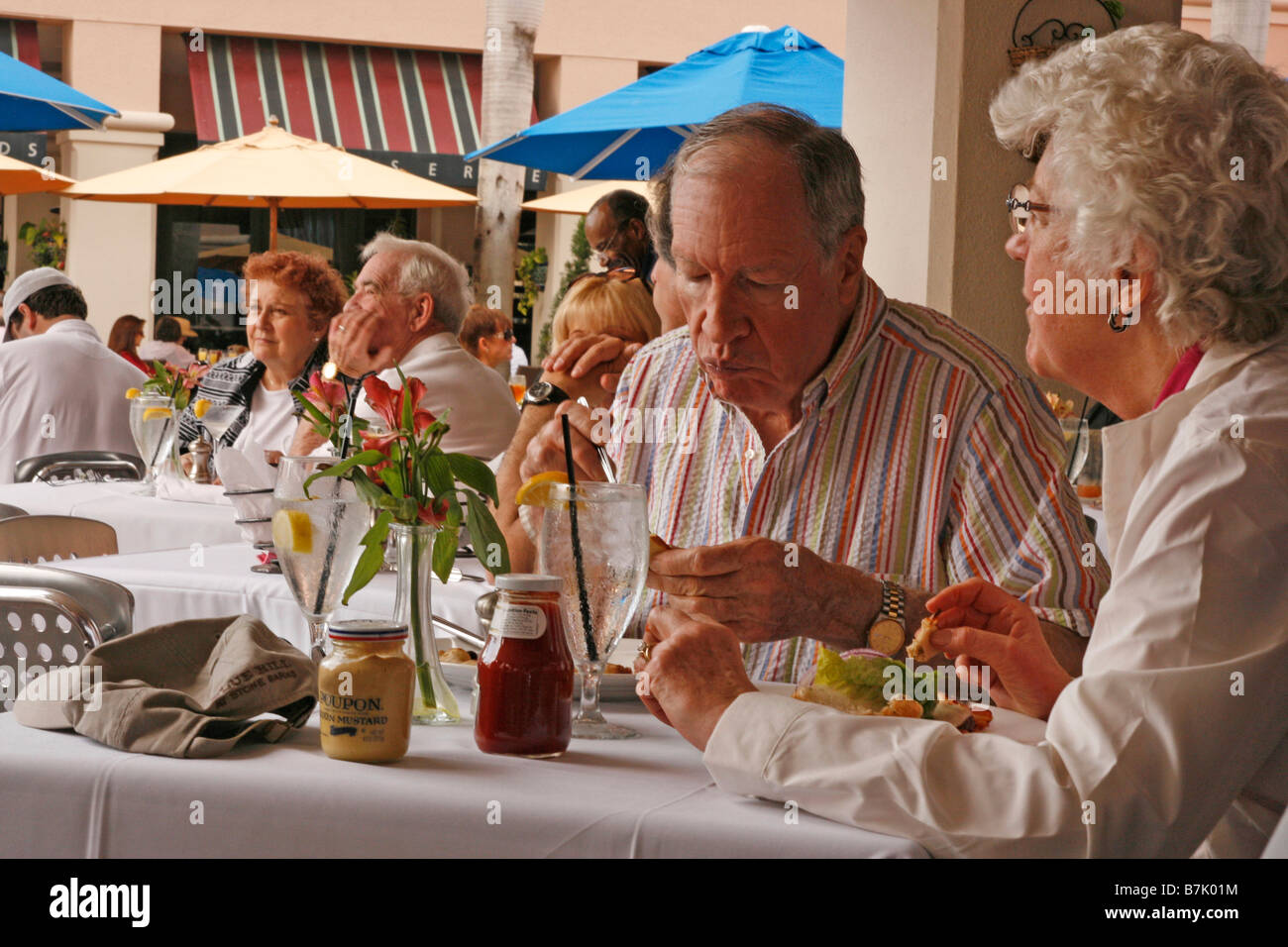 Vieux couple manger le déjeuner à un restaurant en plein air parmi les autres convives. Banque D'Images