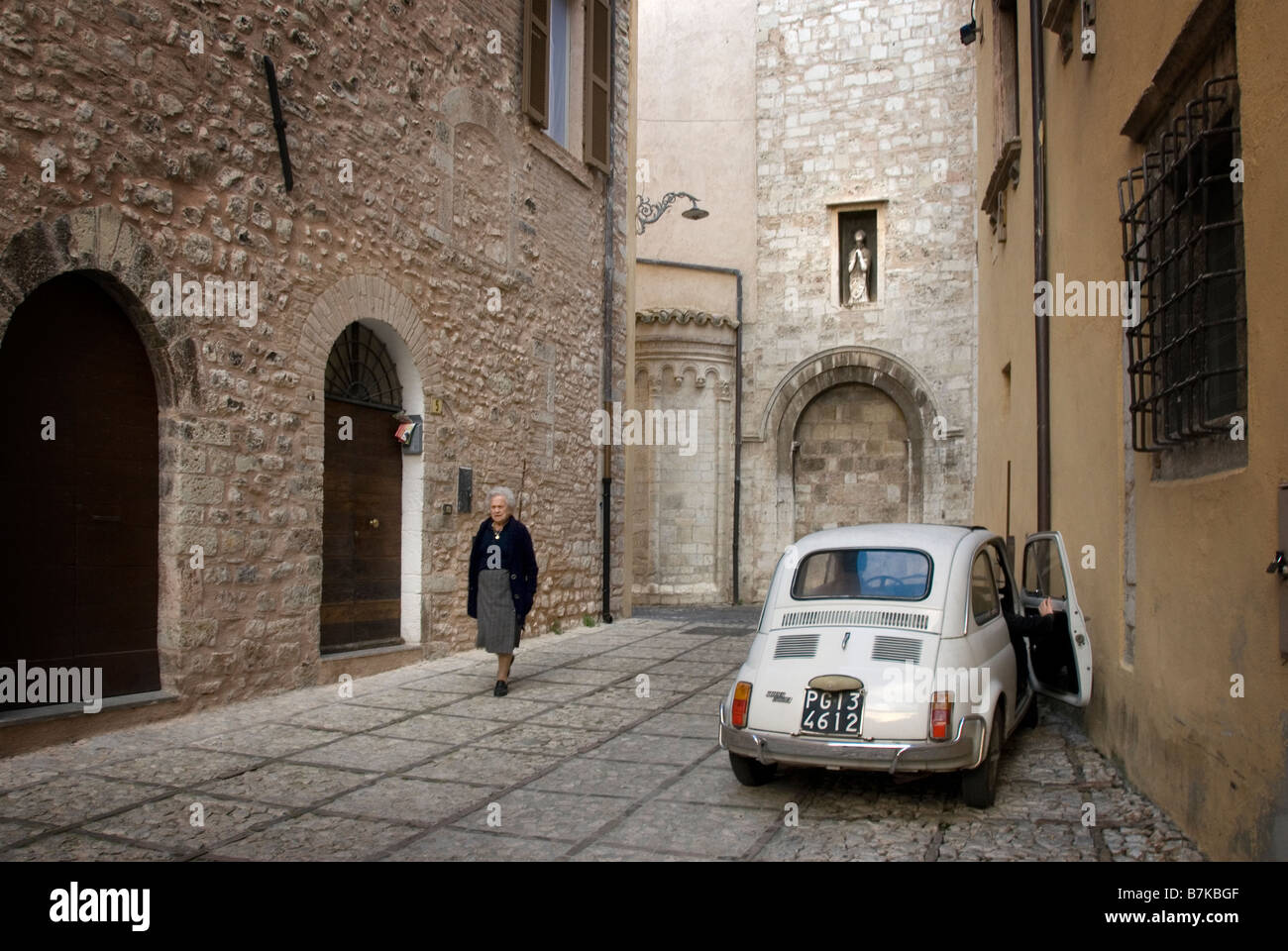 Vieille Femme monte une rue à Trevi, de l'Ombrie, une fiat bambino est stationné. Banque D'Images