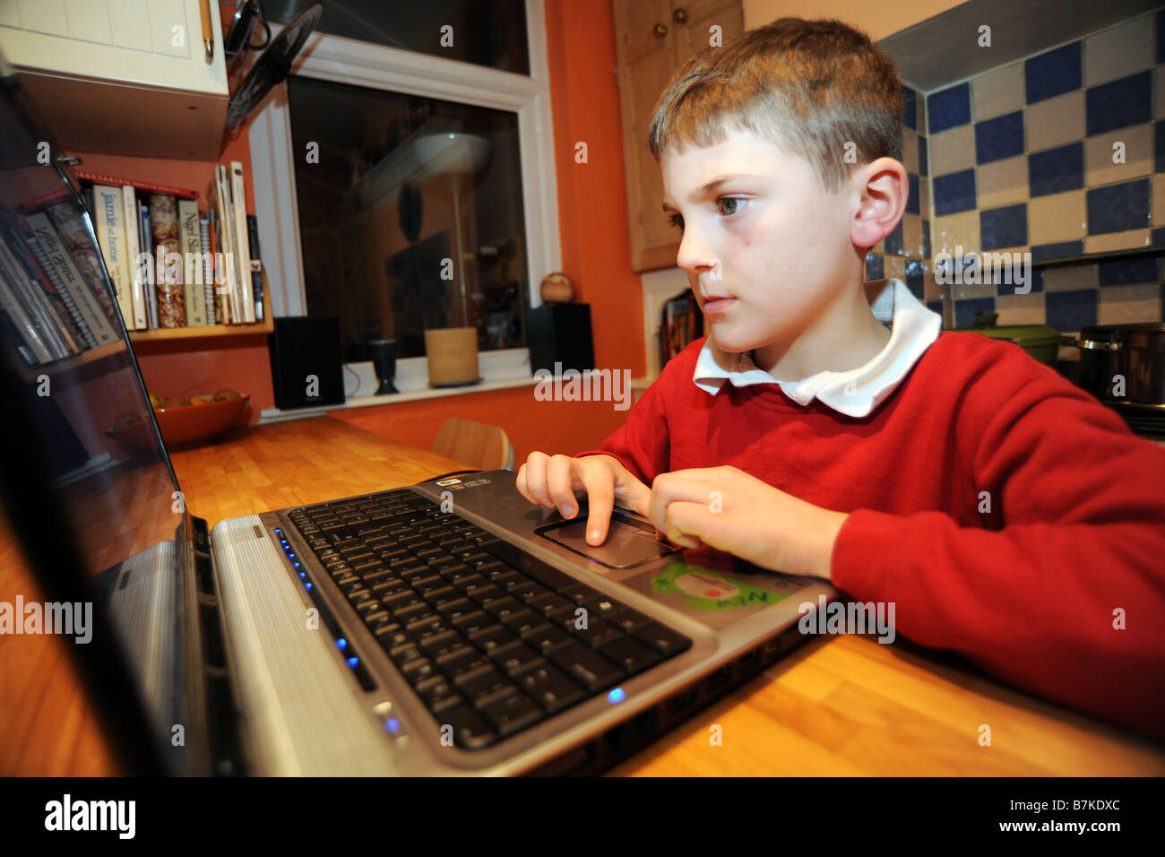 Un garçon de huit ans utilise l'ordinateur portable pour faire ses devoirs dans la cuisine Banque D'Images