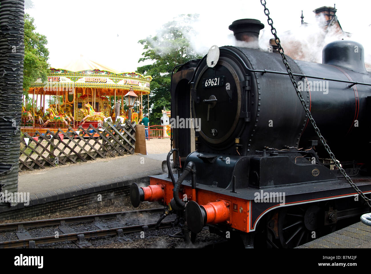 Un moteur à vapeur à Weybourne station avec une foire des chevaux au galop rouler en arrière-plan. Norfolk, Angleterre, Royaume-Uni. Banque D'Images
