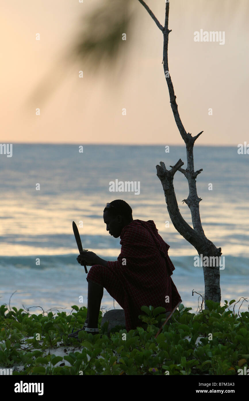 Silhouette d'un homme Masai assis sous un arbre avec un couteau sur une plage à Zanzibar, Tanzanie, Afrique Banque D'Images Silhouette d'un homme Masai assis sous un arbre avec un couteau sur une plage à Zanzibar, Tanzanie, Afrique Banque D'Images
