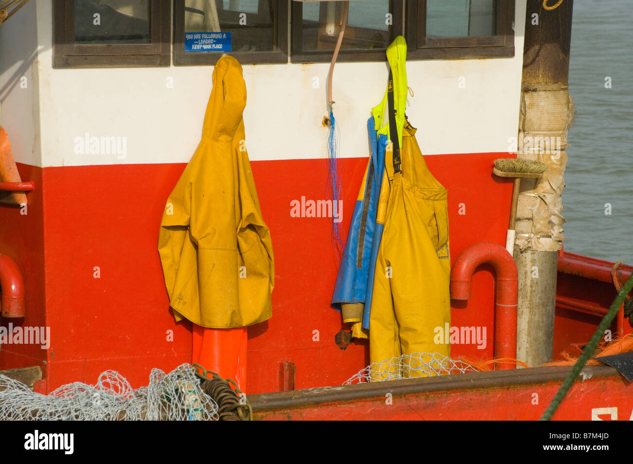 L'imperméable jaune Fishermans accroché sur l'arrière de la timonerie d'un bateau de pêche commerciale Vêtements imperméables Banque D'Images