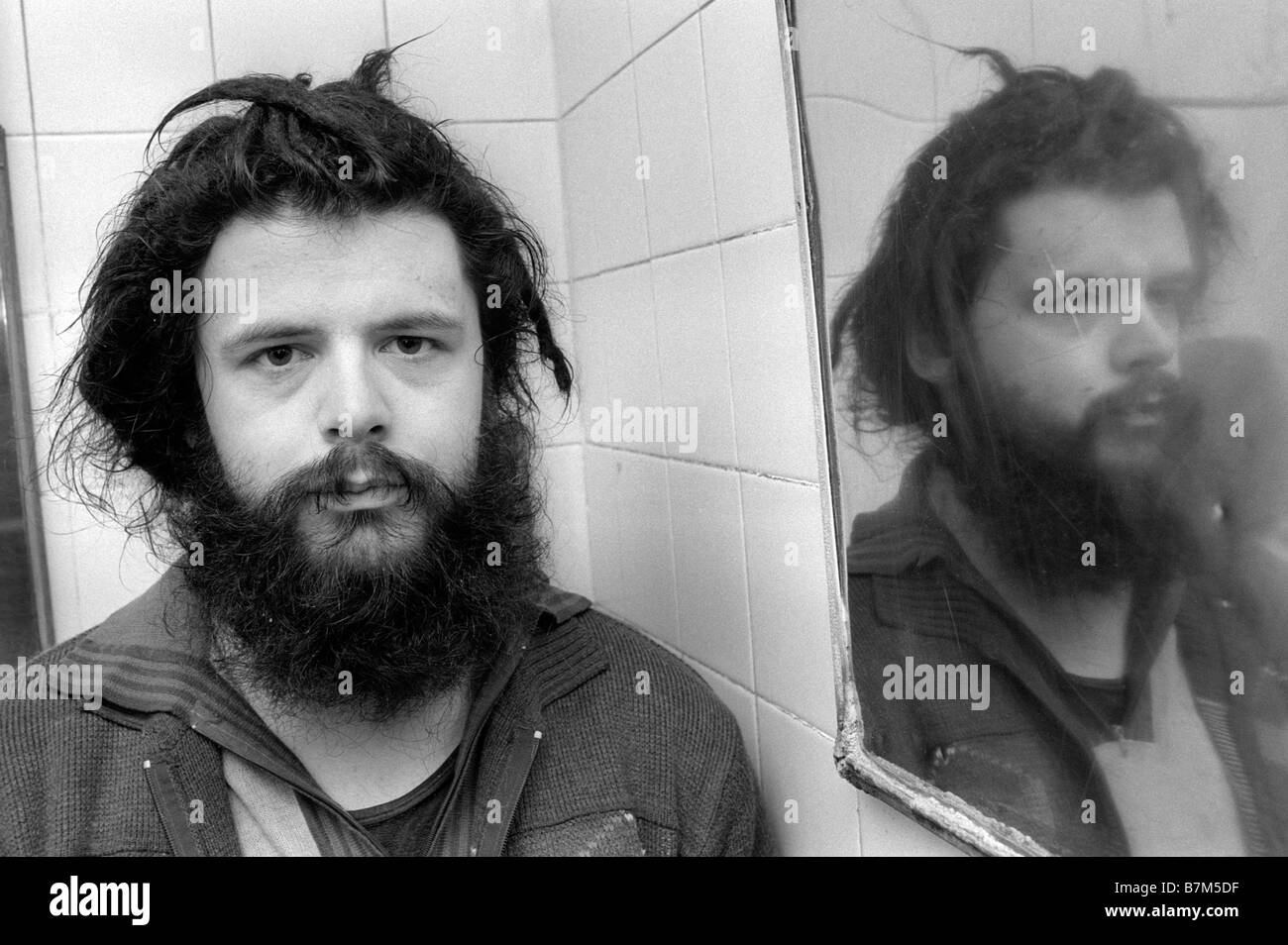 Jeune homme sans-abri avec barbe et cheveux emmêlés en passant la nuit dans une toilette publique pour garder au chaud en hiver UK Banque D'Images Jeune homme sans-abri avec barbe et cheveux emmêlés en passant la nuit dans une toilette publique pour garder au chaud en hiver UK Banque D'Images