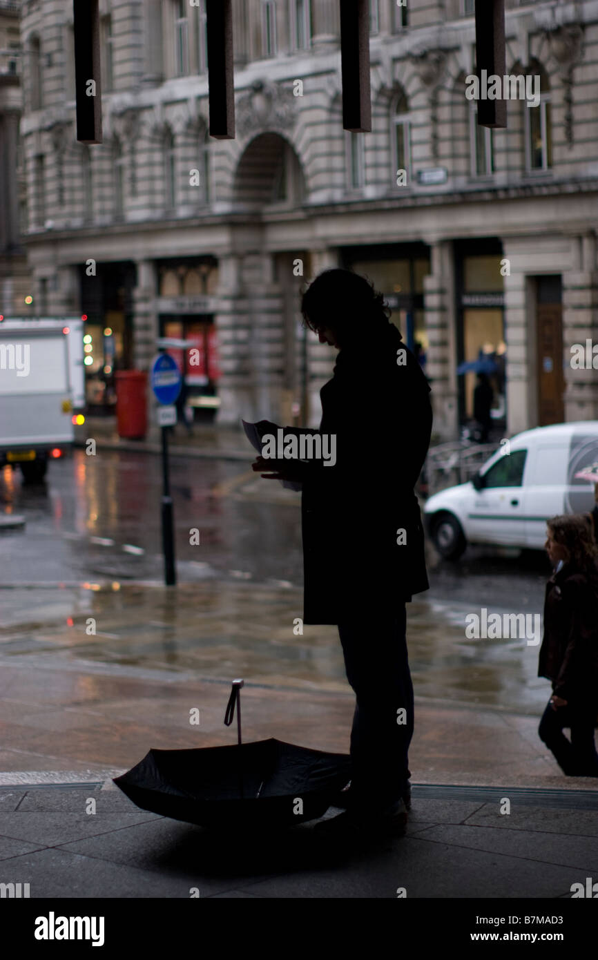 Un jour de pluie dans le quartier financier de Londres, un employé de bureau se met à l'abri d'une averse dans la City de Londres, avec un parapluie posé sur le trottoir Banque D'Images