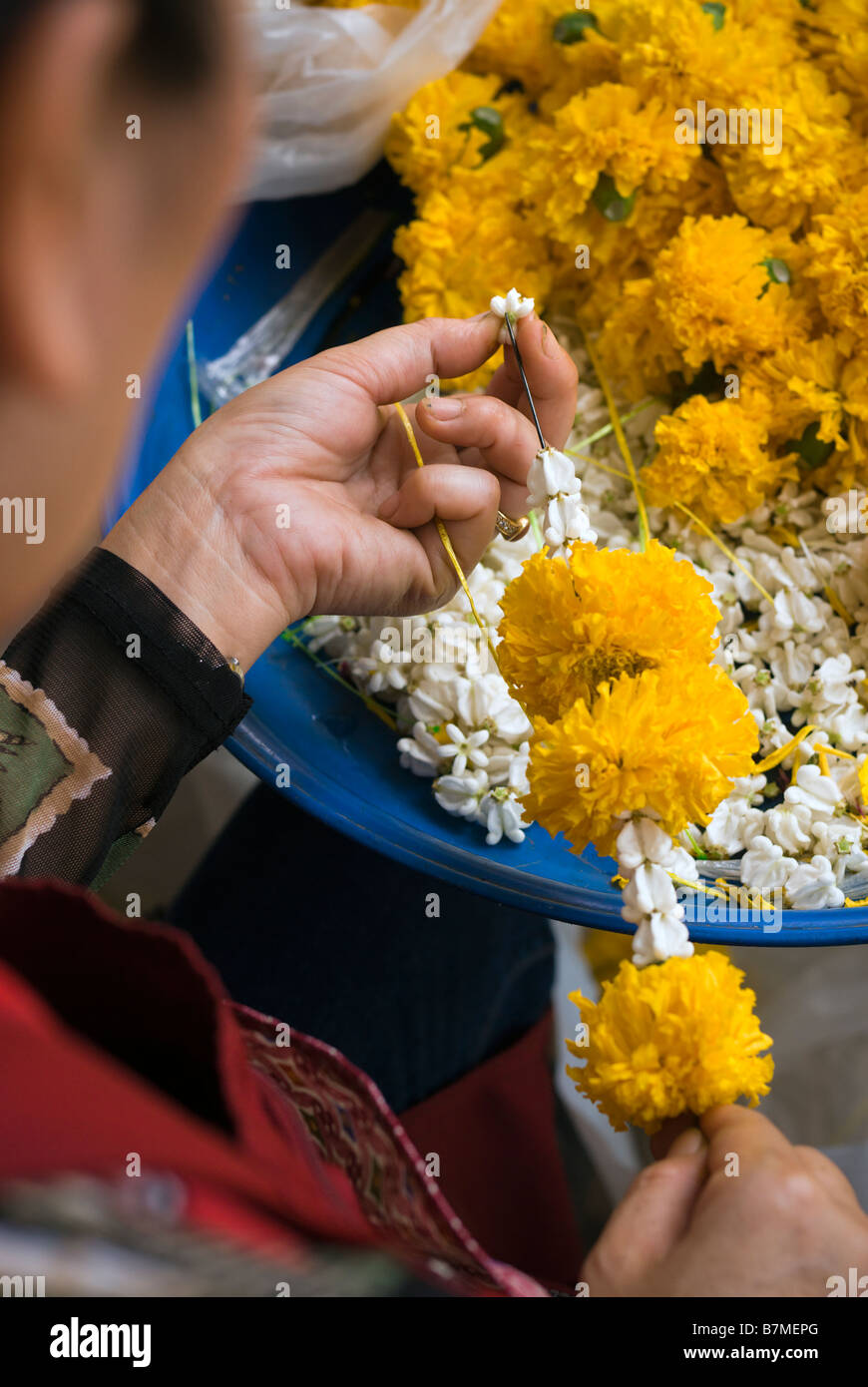 Détail de la femme faisant des offrandes de fleurs de dévotion sur un étal au marché aux fleurs de Pak Khlong Talad Bangkok Thaïlande Banque D'Images