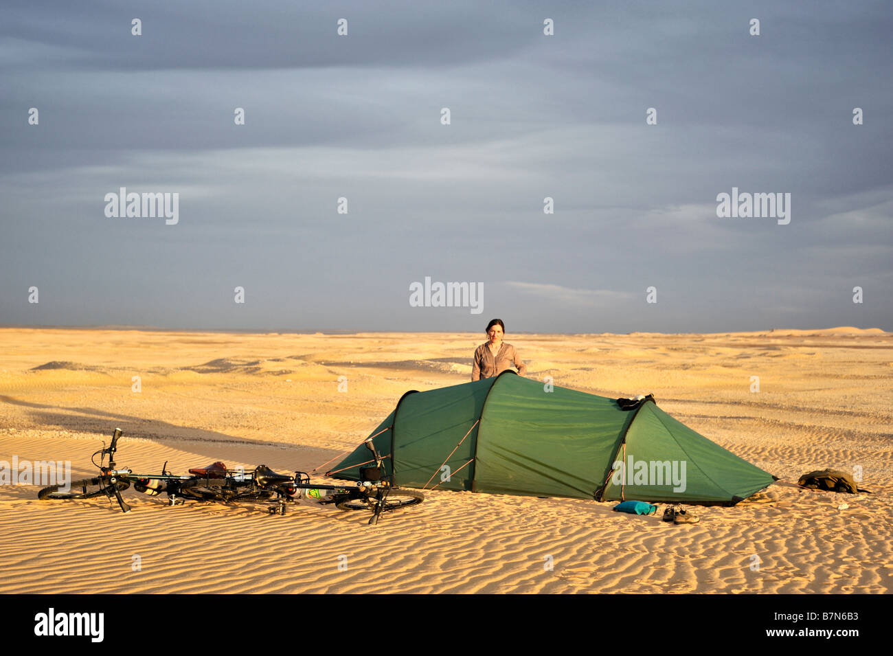 Girl standing next to tente avec les vélos dans la lumière du soir d'or au désert occidental de l'Égypte Banque D'Images