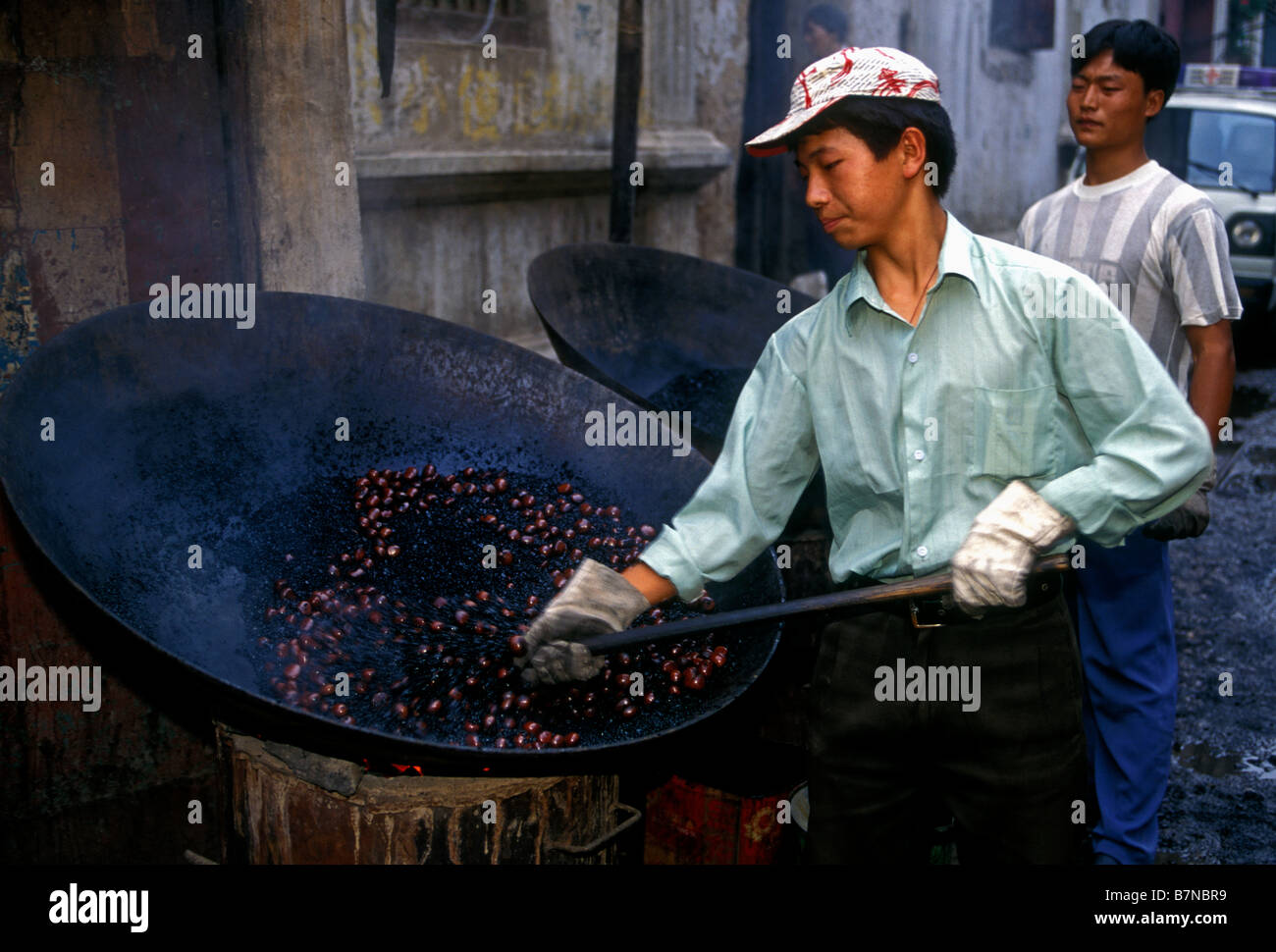 Chinese man, homme adulte, travailleur, travailler, cuisiner les châtaignes, feu de charbon, giant wok, capitale, Kunming, Province du Yunnan, Chine Banque D'Images
