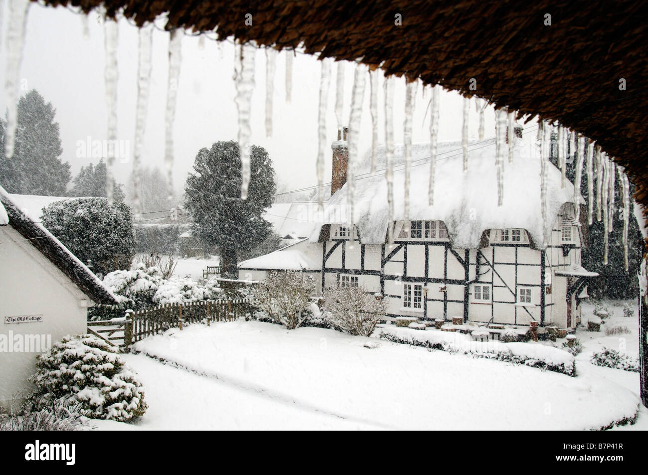 Paysage de neige hiver english country village. Maisons de chaume vue à travers les glaçons suspendus England UK Banque D'Images