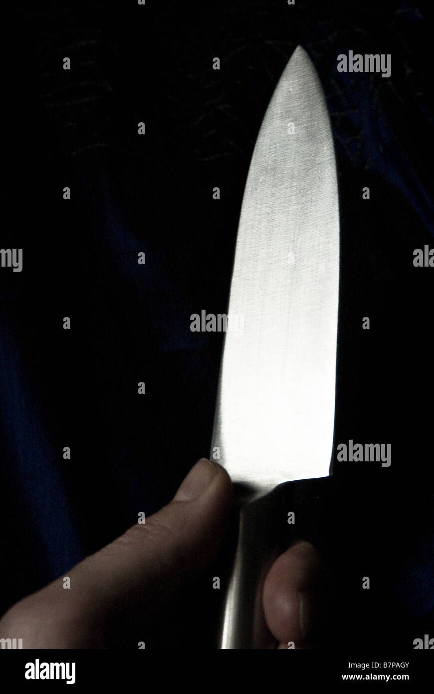La main d'un homme tenant un couteau en métal brillant contre un fond sombre. Banque D'Images