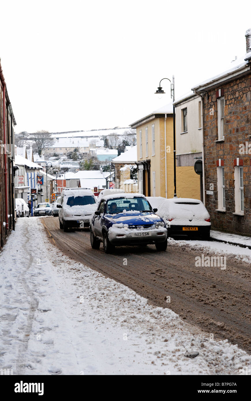 Les voitures qui circulent dans un village rempli de neige Rue à Cornwall, uk Banque D'Images