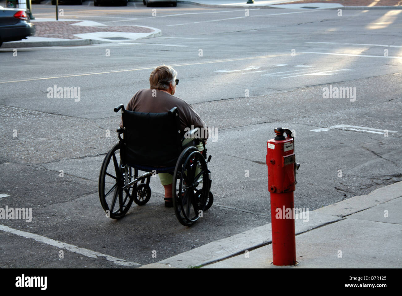 Femme âgée en fauteuil roulant en place de stationnement sur rue pour un tour. Banque D'Images