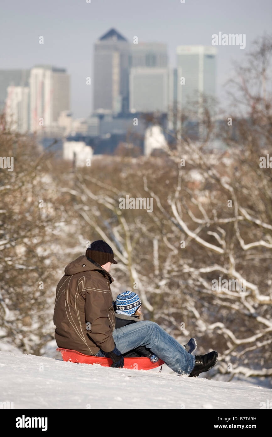 3/2/2009 Le Père et l'enfant la luge en bas de la colline couverte de neige dans le parc de Greenwich avec Docklands dans la distance, London England UK Banque D'Images