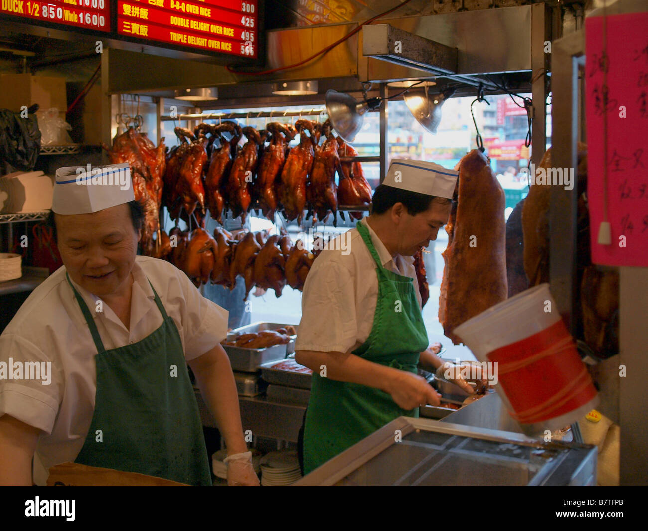 Chefs chinois dans un restaurant chinois dans le quartier chinois de Manhattan entouré de canard rôti, pick, poulet et autres viandes. Banque D'Images