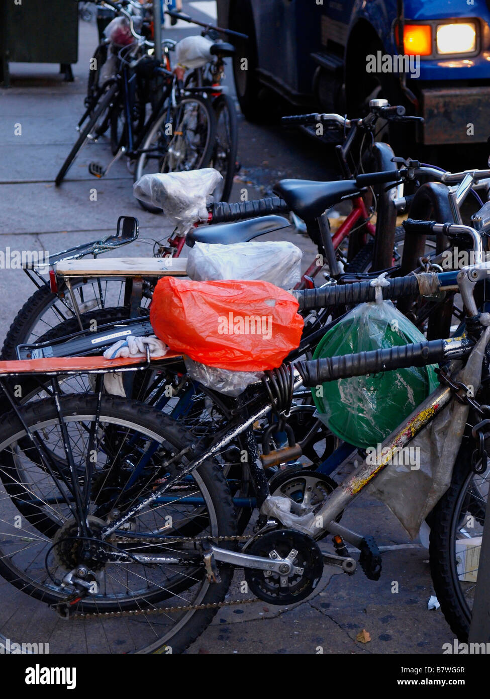 Streetworn et bien utilisé des Bicyclettes avec sièges recouverts de sac enchaîné à un porte vélo près d'une rue animée de la ville de New York. Banque D'Images