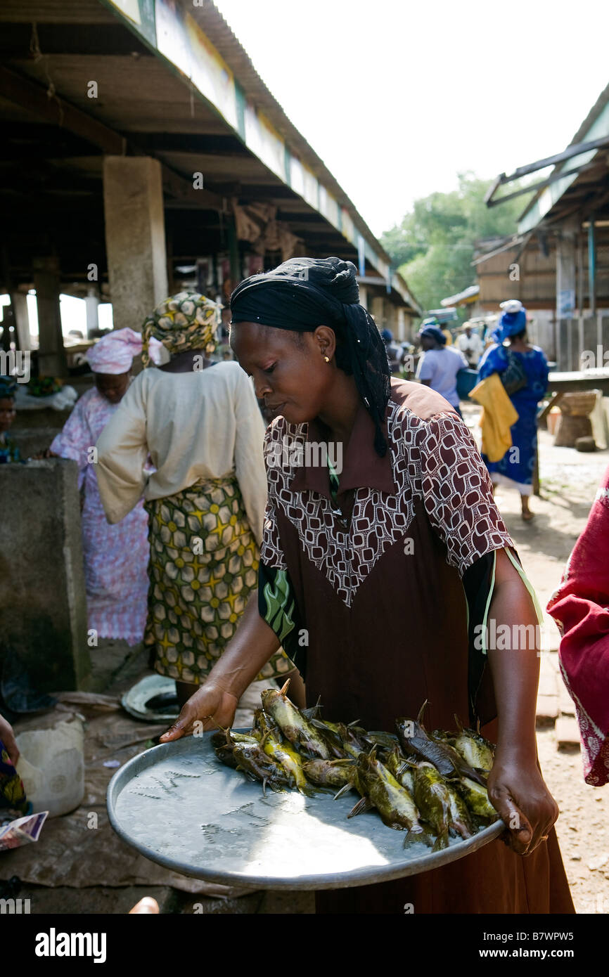Femme porte un plateau de poisson jaune vidé dans un marché de poissons Banque D'Images