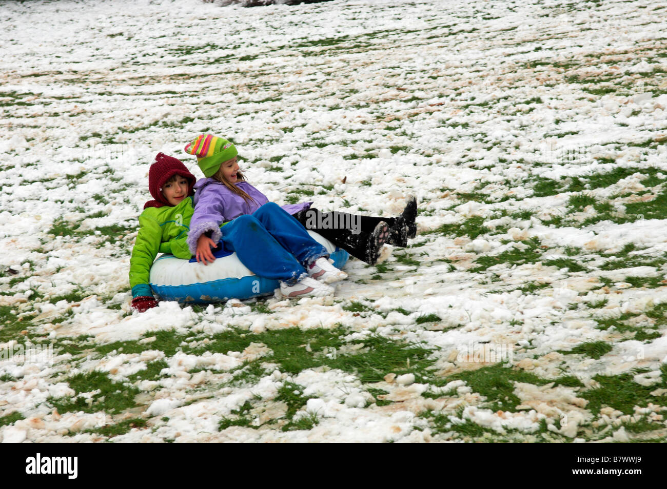 Deux jeunes filles s'amusant faisant glisser en bas de la colline dans la neige UK Banque D'Images