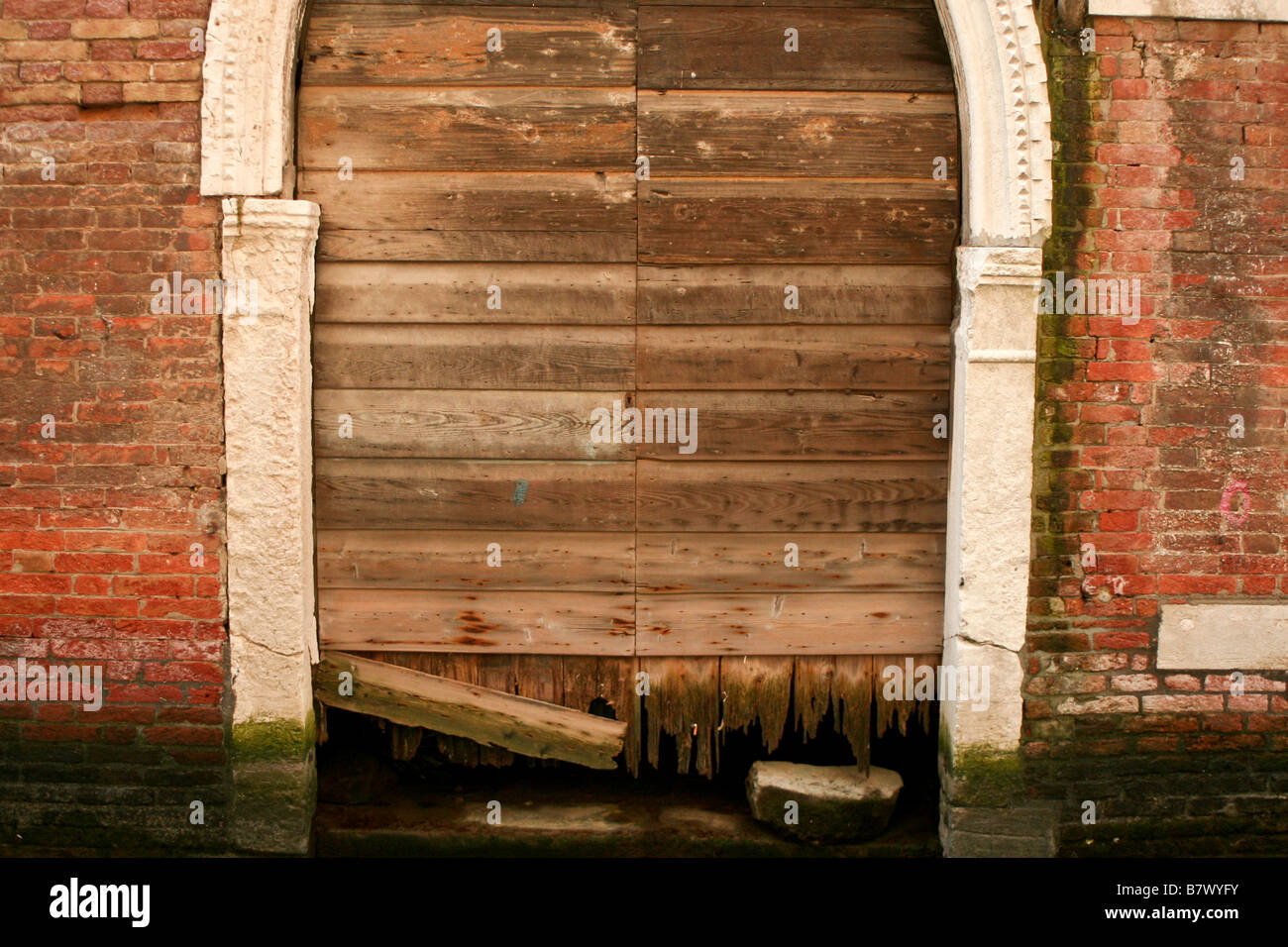 Un bateau cassé porte dans un canal vénitien entouré par un mur de briques rouges couverts d'algues et de moisissures. Banque D'Images