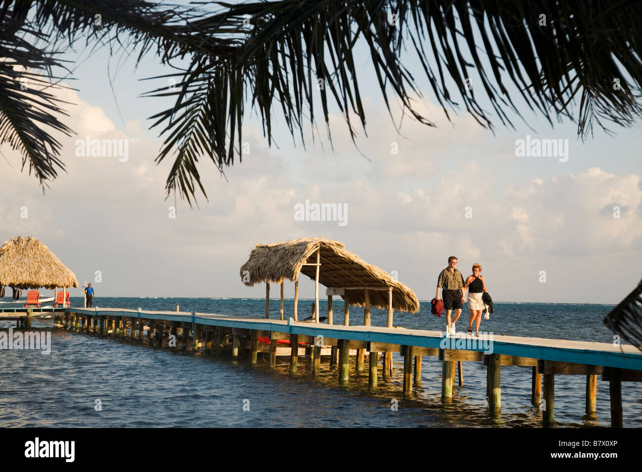 Couple d'Ambergris Caye BELIZE descendre pier vers restaurant des toits de chaume sur les structures du quai des eaux des Caraïbes palmier Banque D'Images