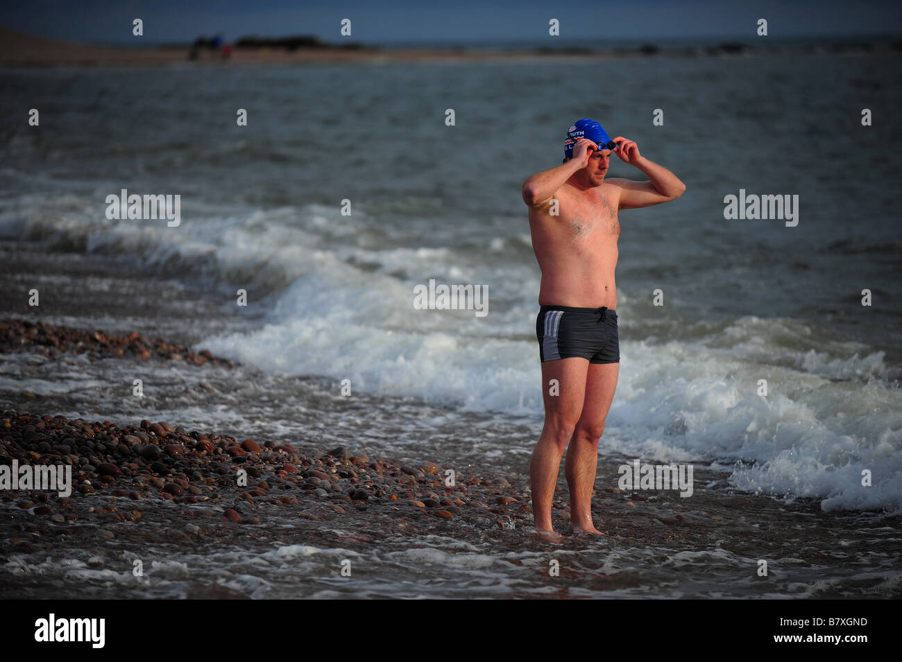 Un homme qui marche dans la mer à la plage avant la baignade à Budleigh Salterton, Devon, UK. Banque D'Images