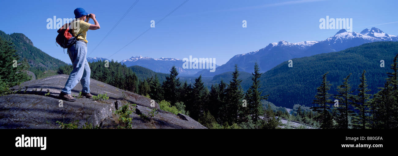 Un randonneur regardant à travers des jumelles à la vue de la chaîne de montagnes de Tantalus près de Whistler et de Squamish, British Columbia Canada Banque D'Images