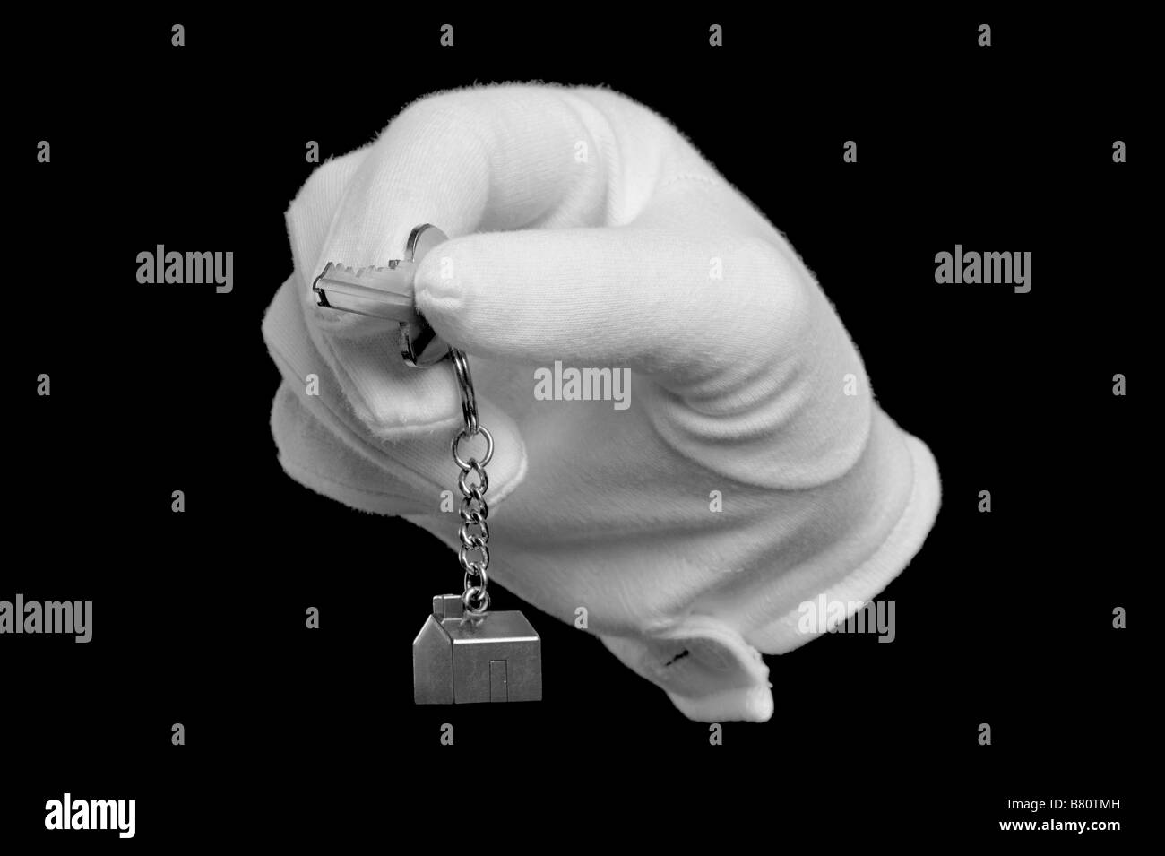 Une main dans un gant blanc tenant la clé d'une nouvelle maison isolated on black Banque D'Images