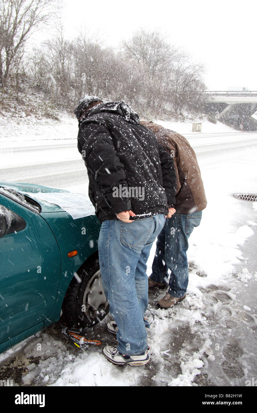 Deux hommes la lecture du manuel d'utilisation d'un ensemble de chaînes à neige pour les mettre sur la roue avant d'une voiture Banque D'Images