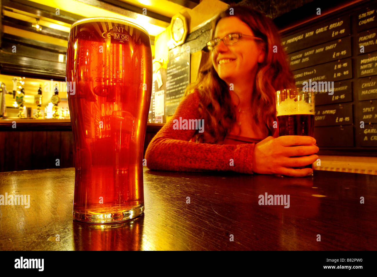 Une jeune femme souriante et tenant une pinte de bière dans un pub Banque D'Images