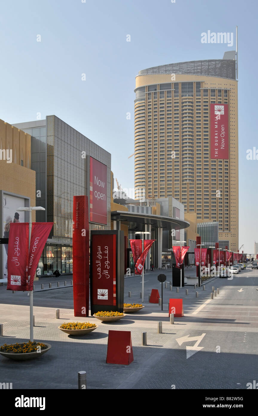 Accès aux routes et bannières rouges avec jardinières à l'extérieur du Complexe commercial Dubai Mall avec bâtiment de grande hauteur au-delà de United Émirats arabes Unis Banque D'Images