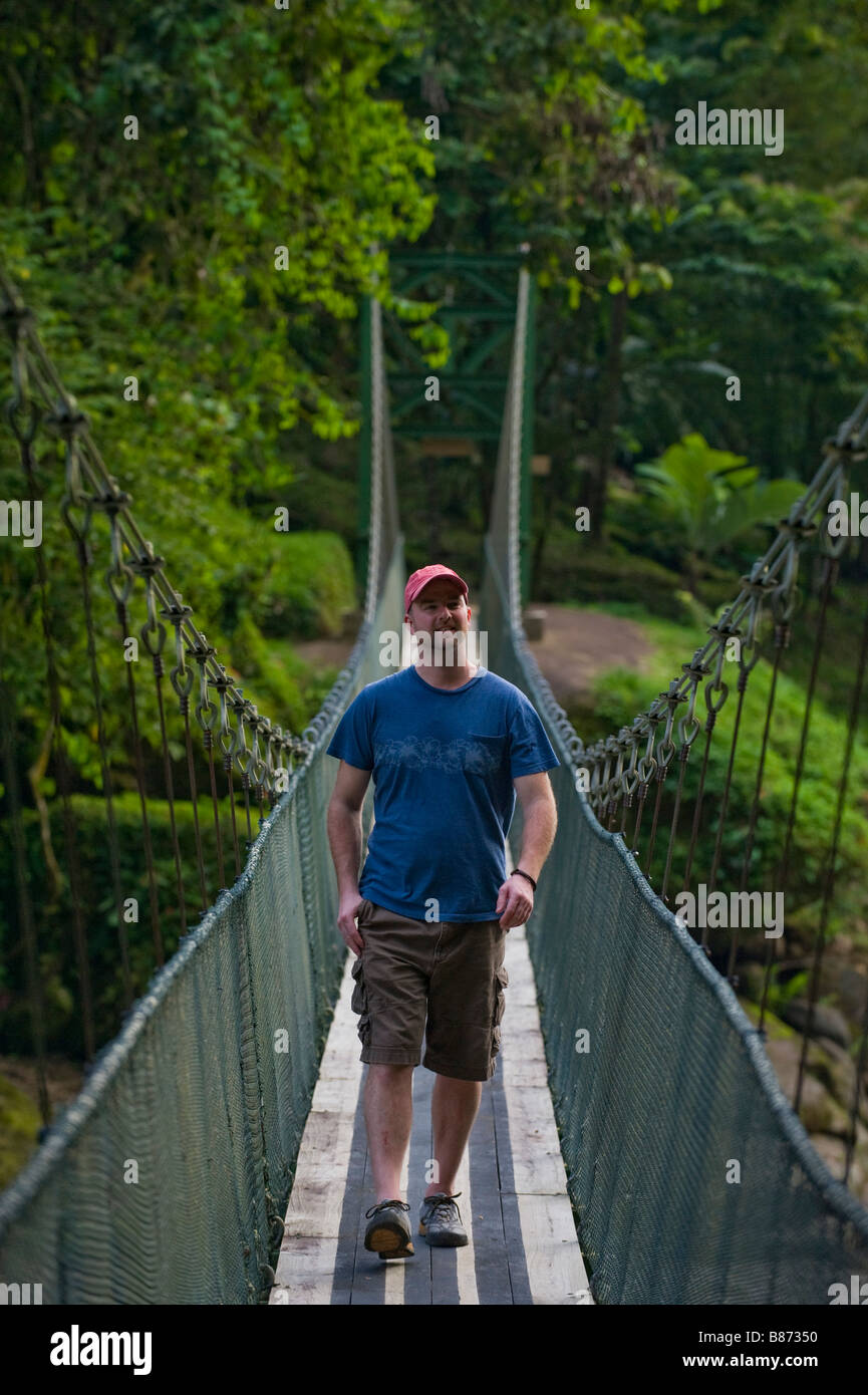 L'Amérique centrale, le Costa Rica. Un homme marche sur la rivière Pacuare sur un pont suspendu. Banque D'Images