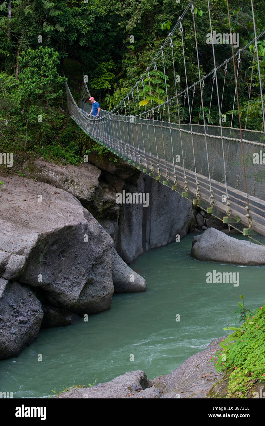 L'Amérique centrale, le Costa Rica. Un homme marche sur la rivière Pacuare sur un pont suspendu. Banque D'Images
