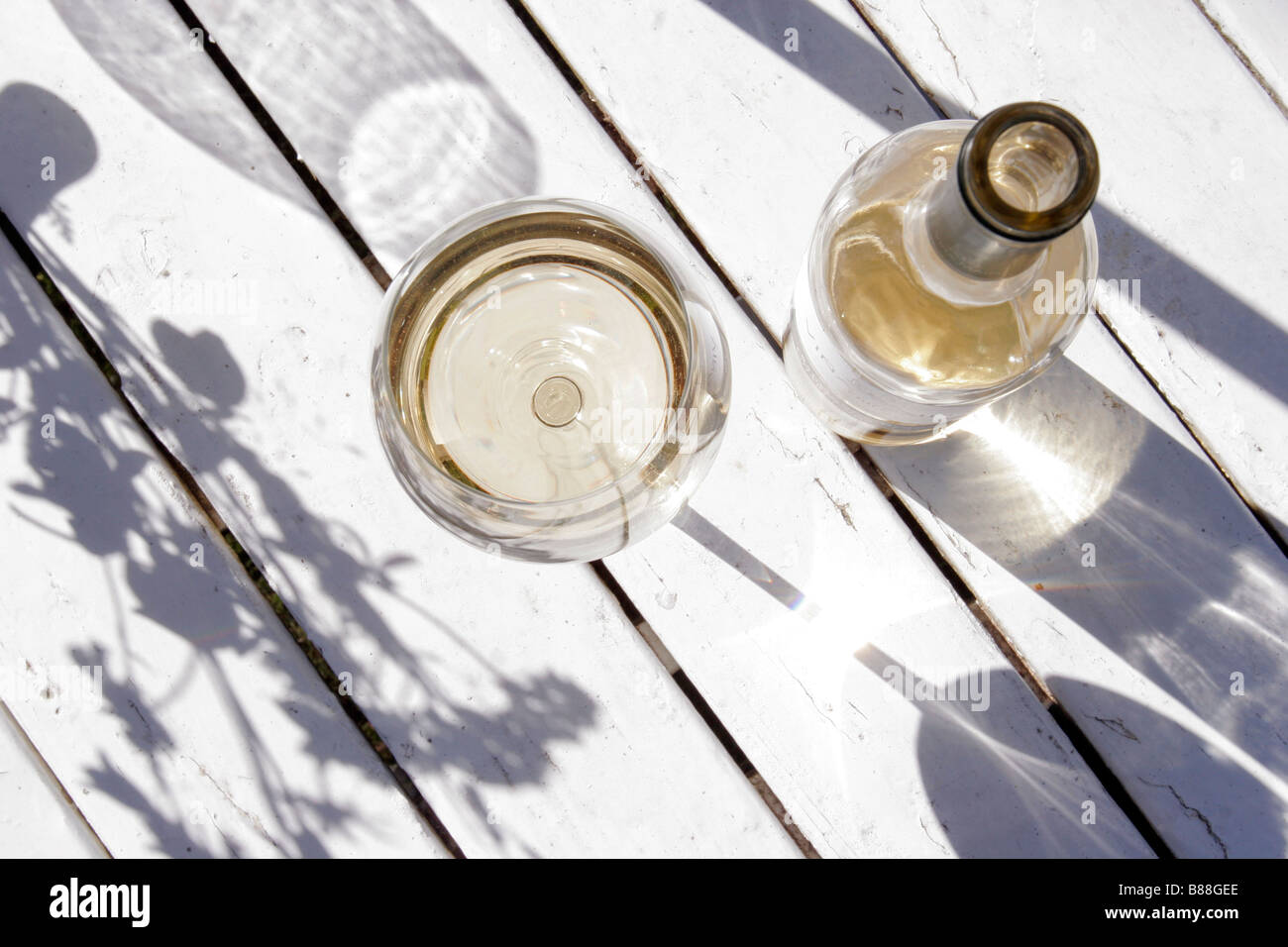 Une bouteille de vin blanc et un verre placé à l'extérieur sur une table en bois blanc. Banque D'Images
