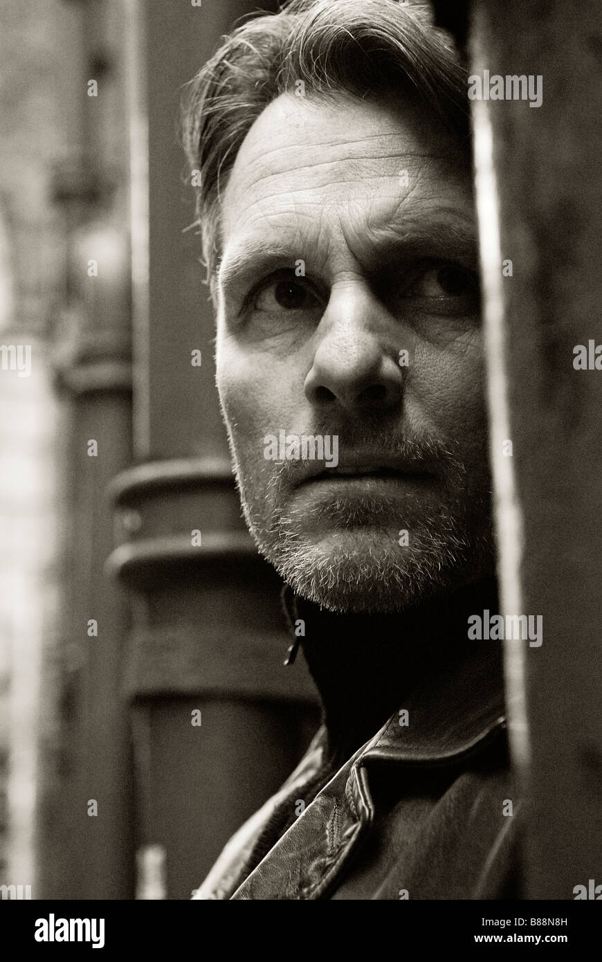 Une sinistre à la quarantaine homme portant une veste en cuir est espionnage sur quelqu'un et de les suivre dans une ruelle. backstreet Banque D'Images