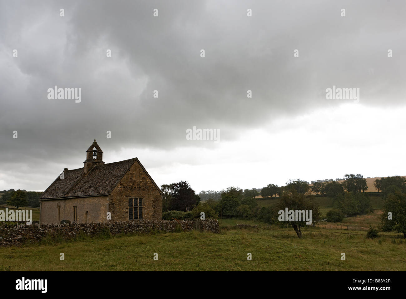 Dans la pluie sous ciel gris derrière un mur en pierre sèche Cotswold - st oswald's Church Windrush Valley Cotswold Hills Banque D'Images