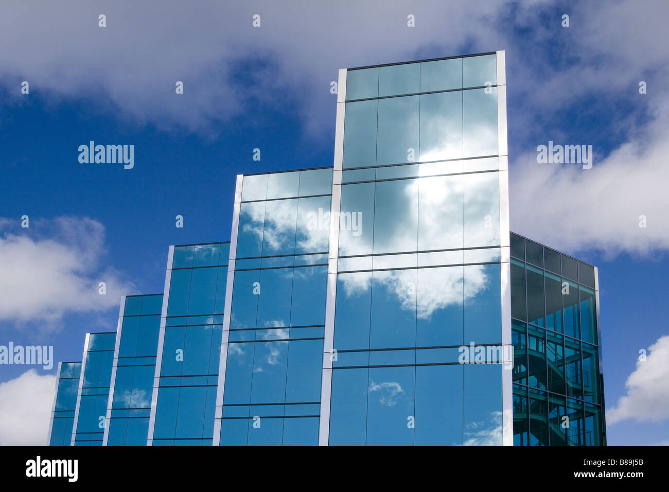 Cinq tours d'un immeuble de bureaux en verre moderne élégant avec des nuages et du ciel réfléchissant sur la surface des bâtiments Banque D'Images