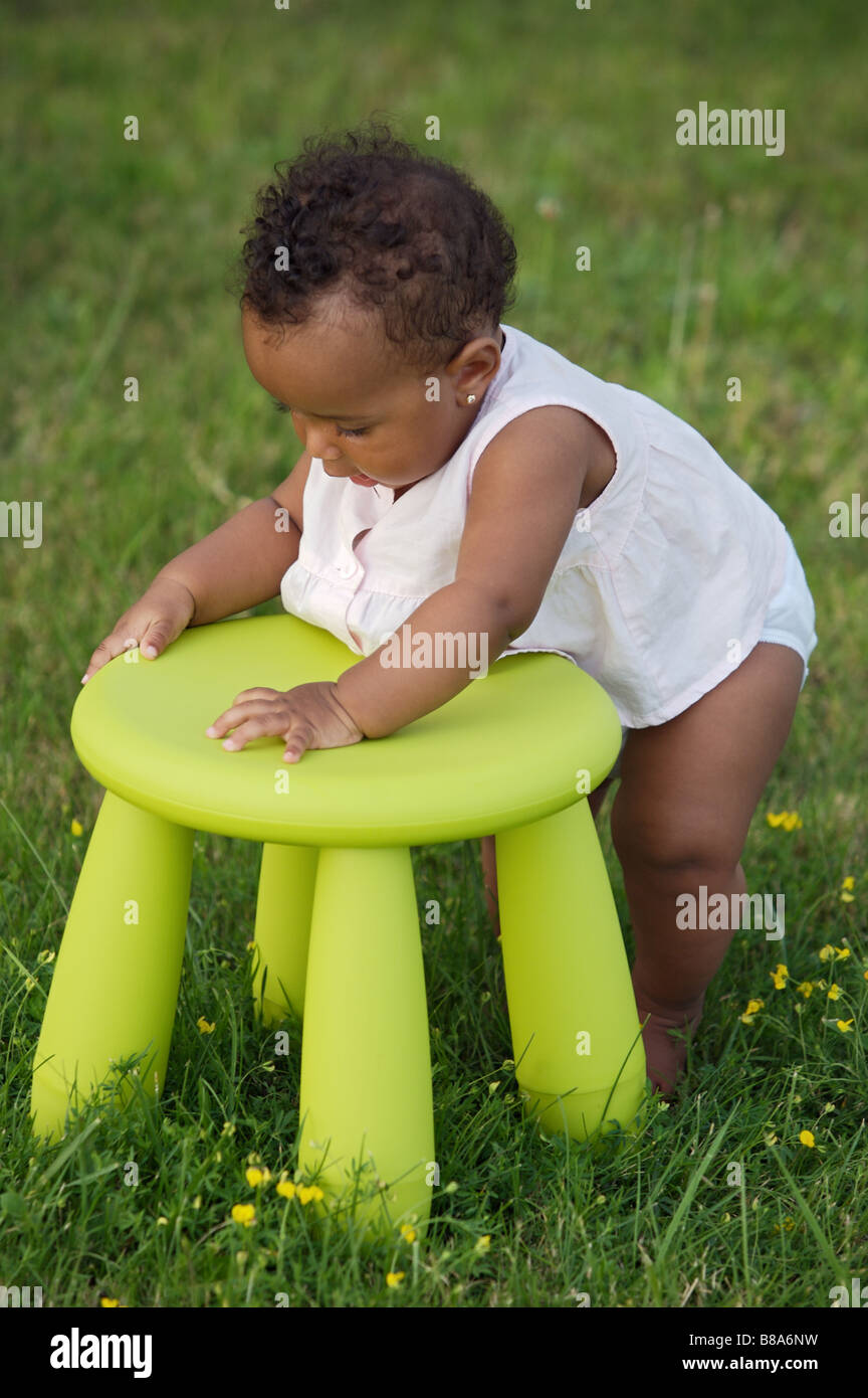 Adorable bébé jouant avec une chaise dans le jardin Banque D'Images