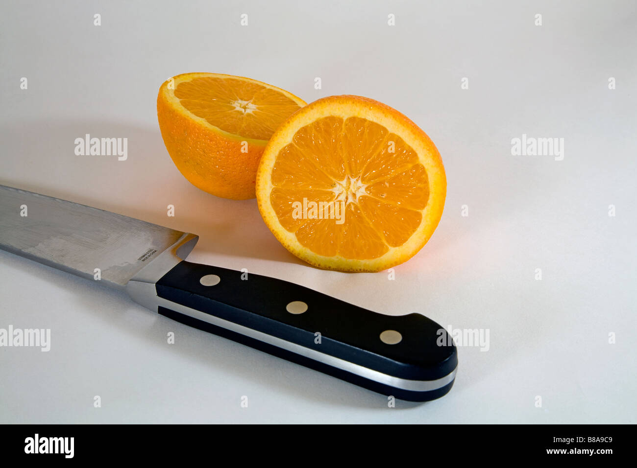 Nature morte de légumes fruits deux moitiés d'une orange Navel uniformément tranchés en deux par un grand couteau de boucher ou de cuisine Banque D'Images