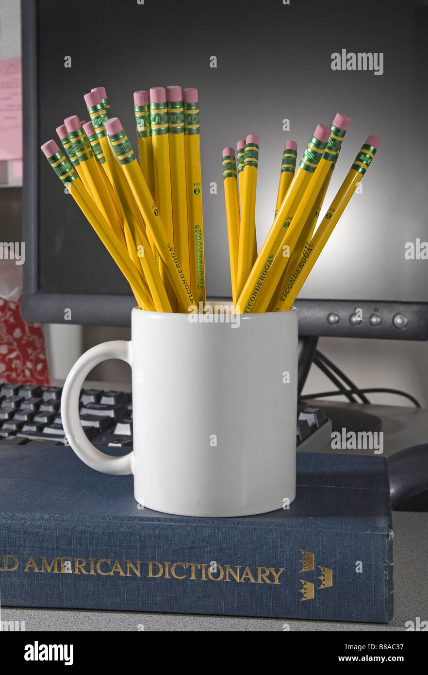 Une tasse ou mug de numéro 2 Ticonderoga plomb ou gommes et crayons graphite devant un ordinateur et assis sur un dictionnaire Banque D'Images