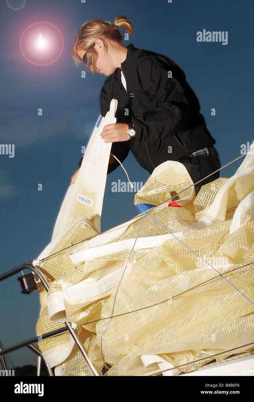 Jeune fille d'environ 25 ans pliage de la voile à bord d'un voilier. Banque D'Images