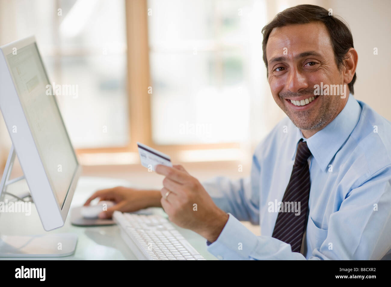 Smiling man shopping online with credit card and computer Banque D'Images